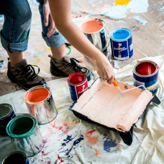 Interior painting supplies with open paint cans and roller tray on protective floor covering