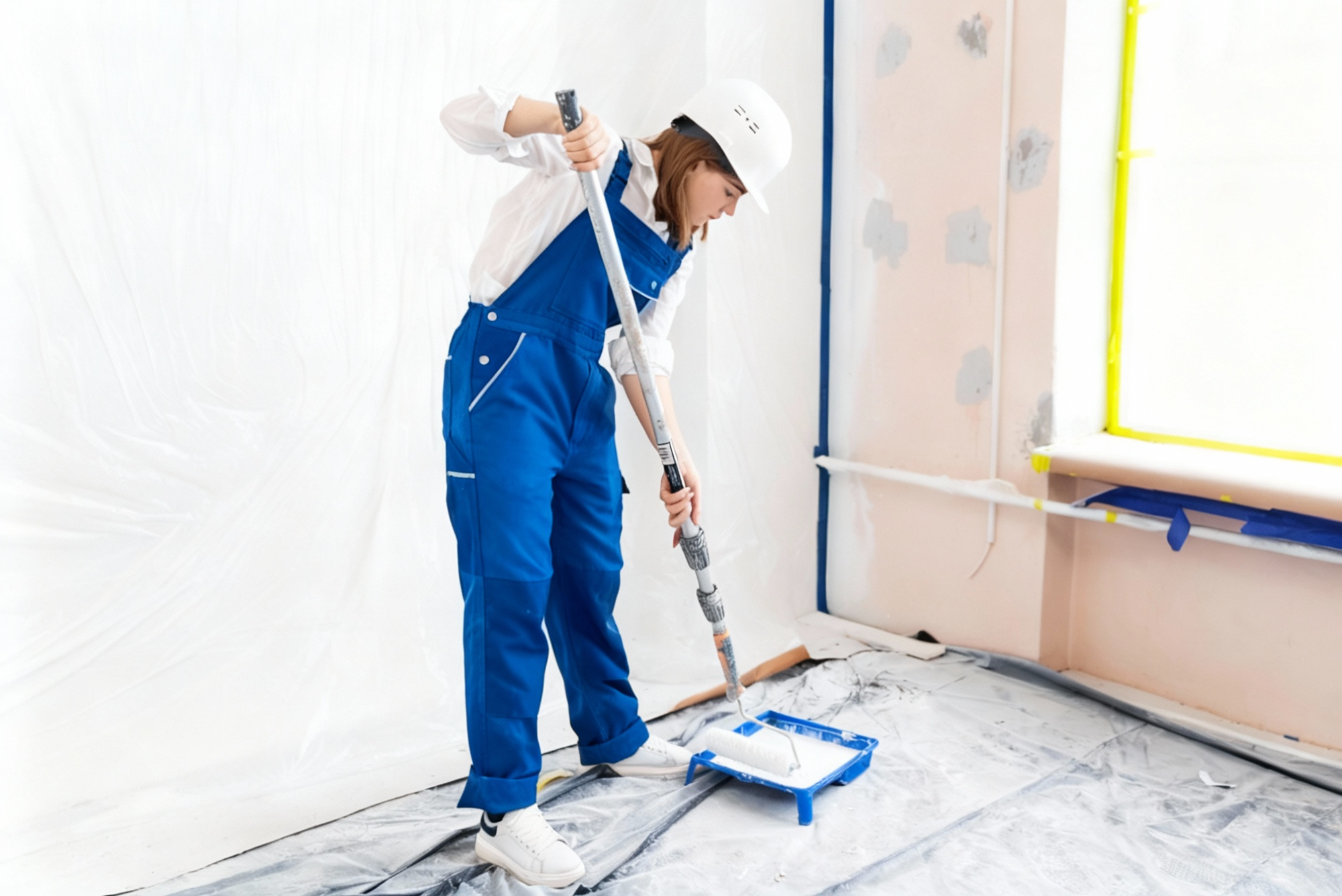 Female painter wearing safety gear and preparing a paint roller during an interior painting project