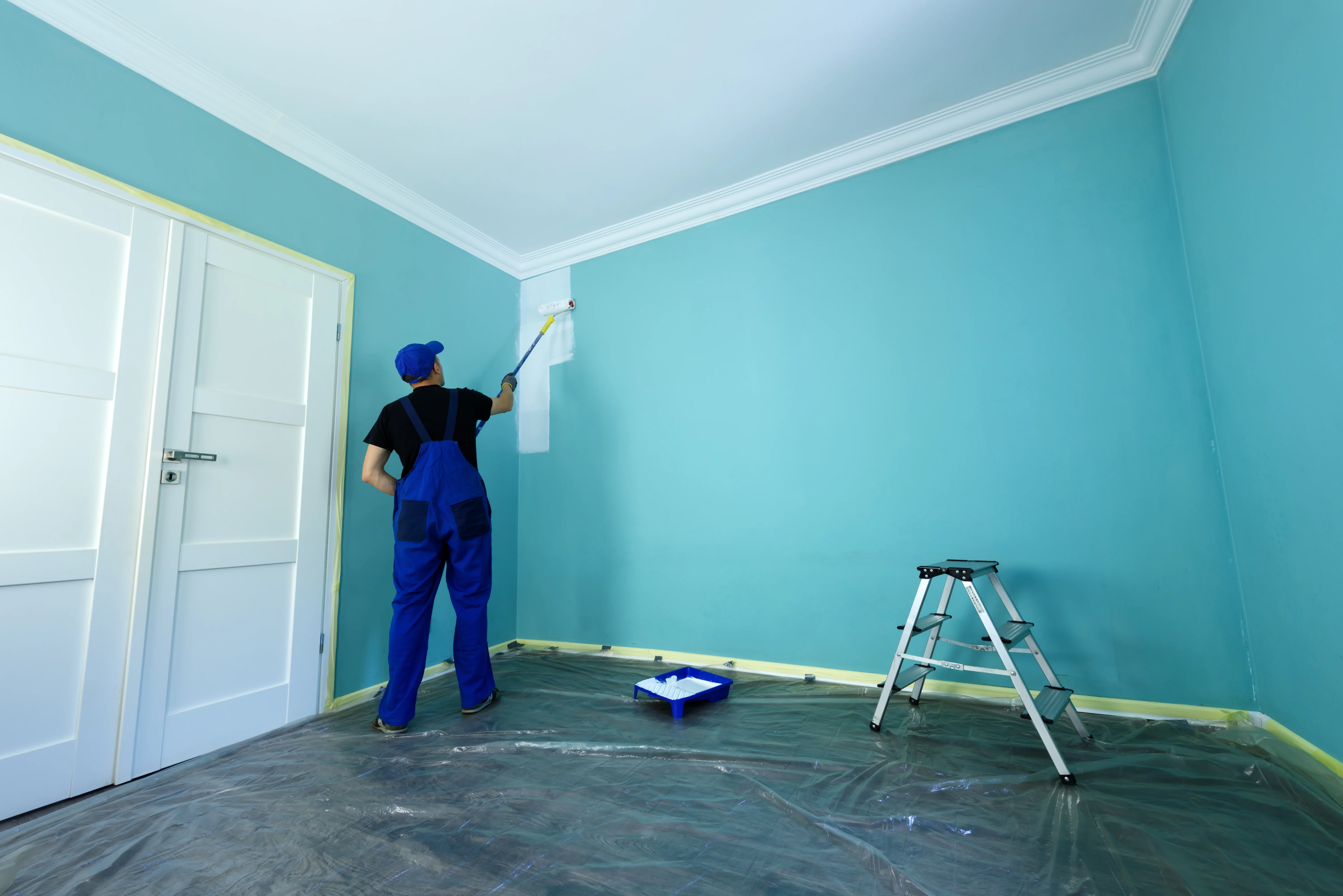 Professional interior painter applying white paint on a turquoise wall with a roller