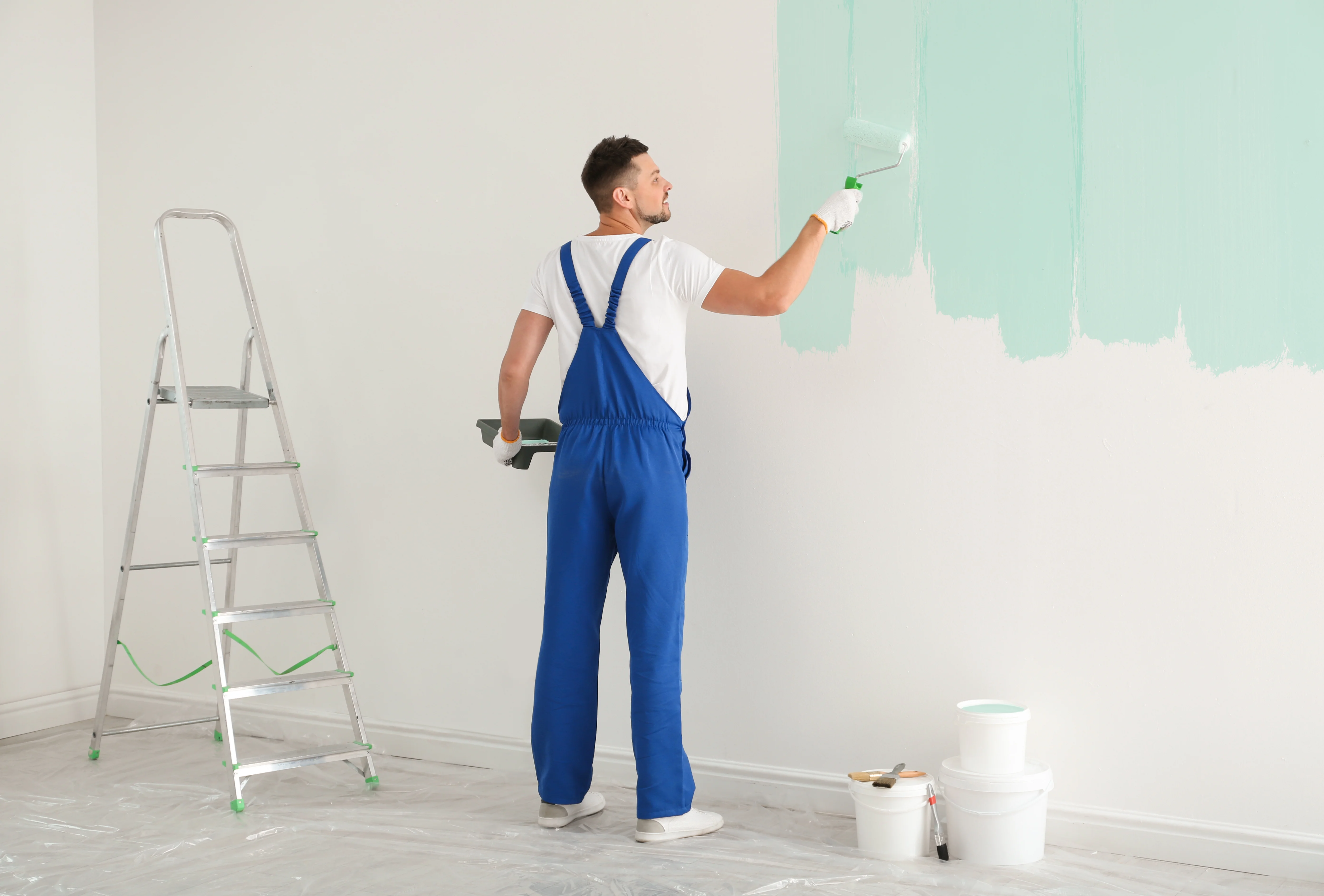 Residential painter applying mint green paint to a white wall during home interior painting