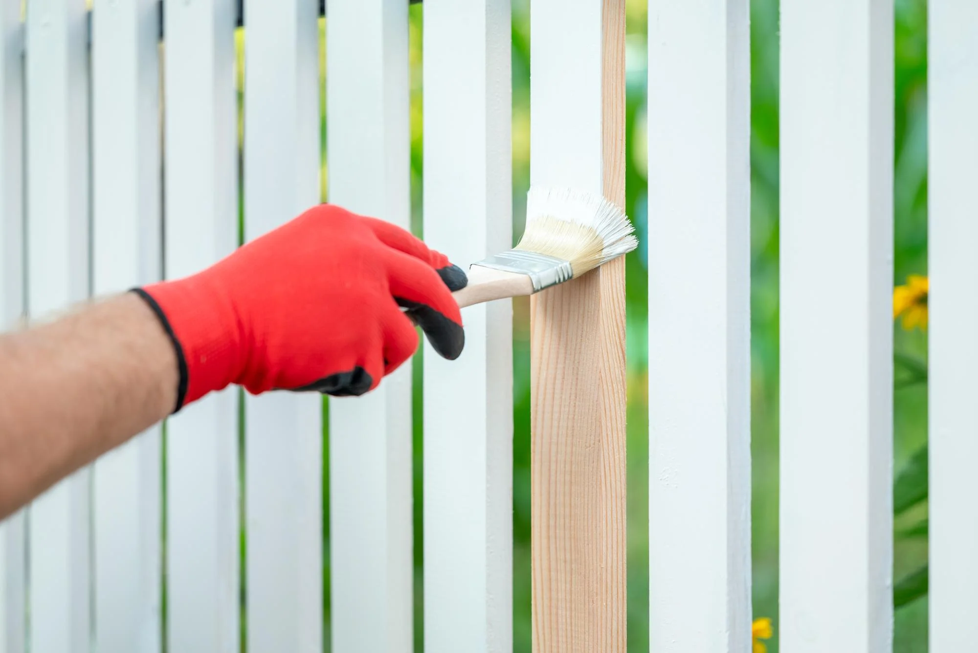 Worker painting a wooden fence with a brush during an exterior fence painting project