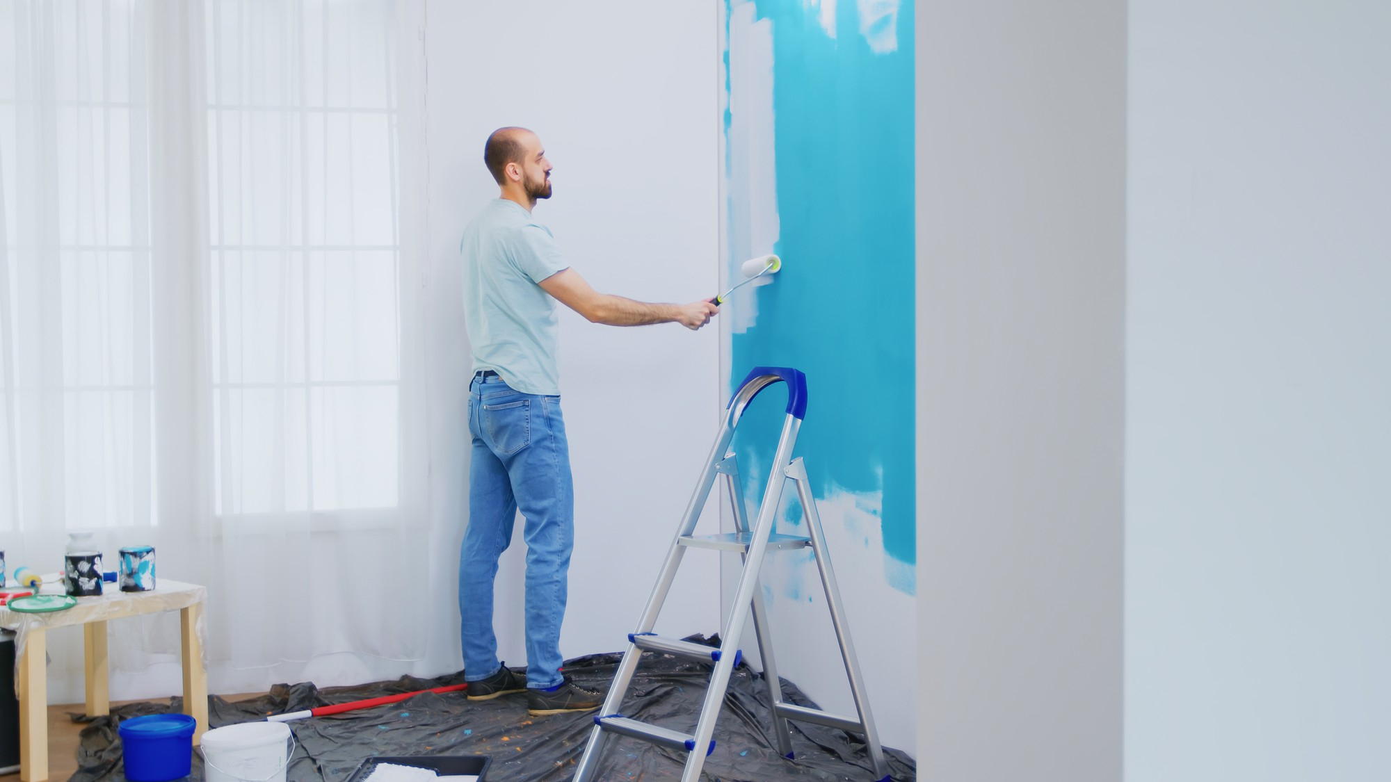 Man painting an interior wall with blue paint during a home renovation project