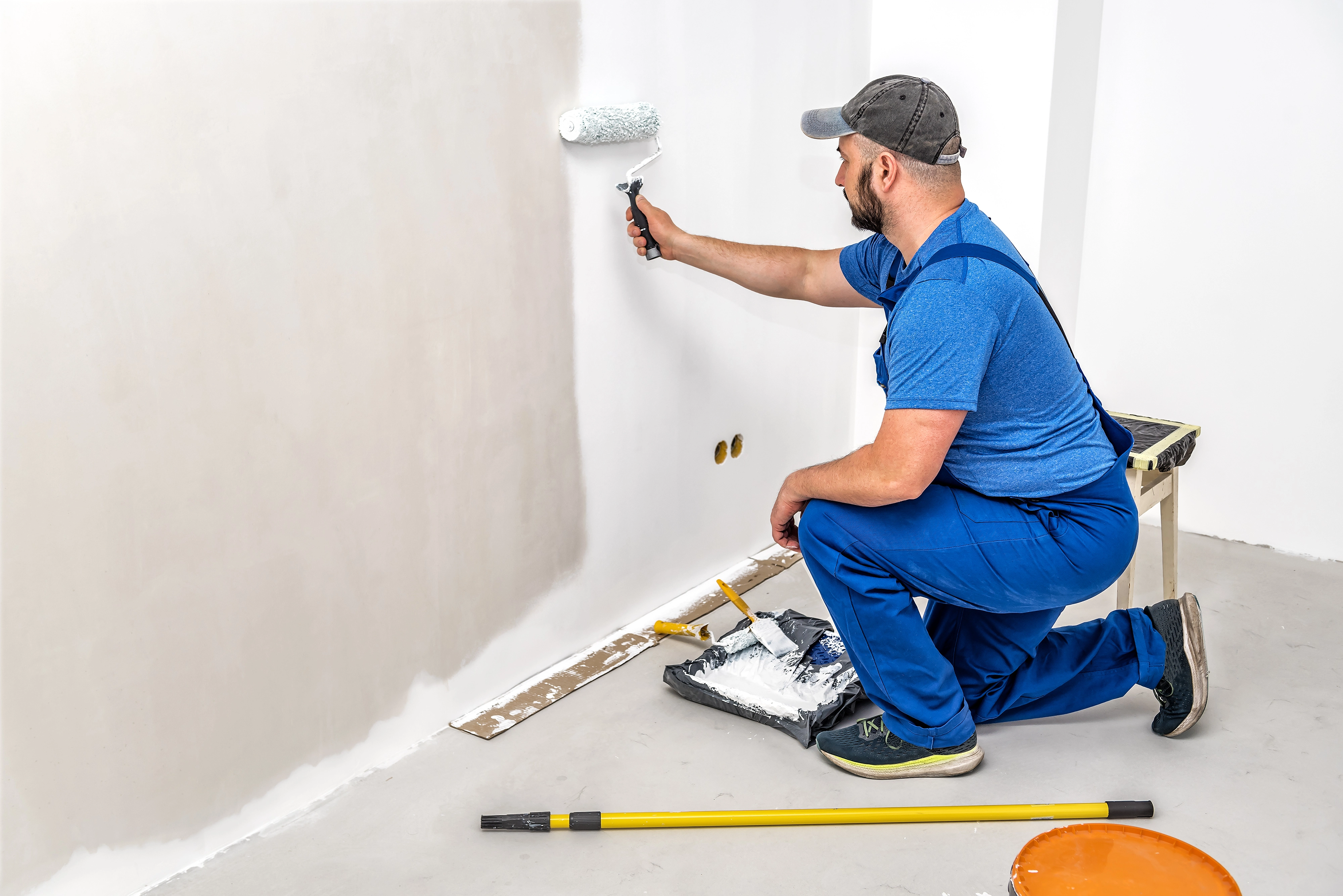 Interior house painter applying white paint to a wall during home renovation
