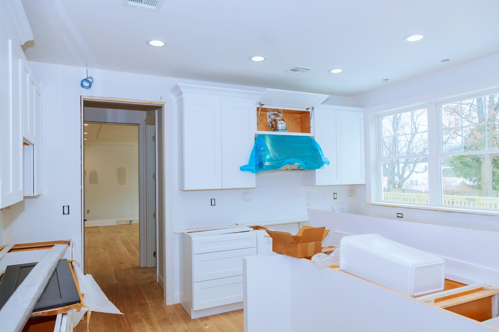 Kitchen renovation in progress with white cabinets being prepared for painting