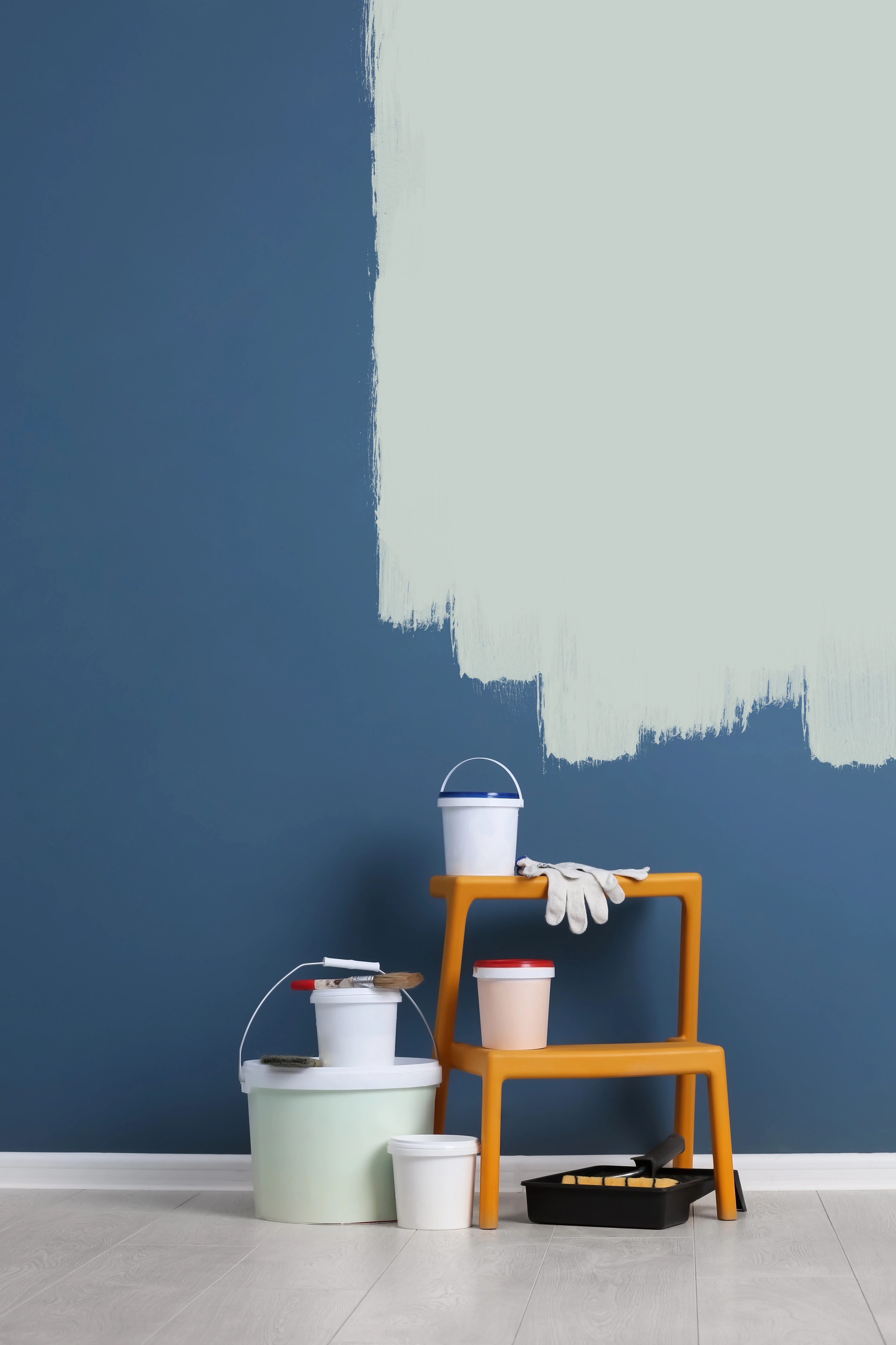 Interior wall painting in progress with paint buckets, roller tray, gloves, and partially painted blue wall, professional home painting service setup